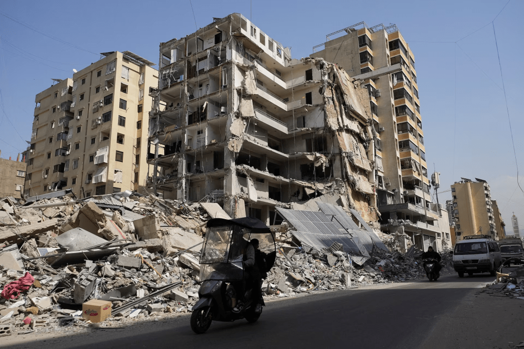 People ride a scooter next to a damaged building in the aftermath of Israeli strikes, amid an escalation between Hezbollah and Israel, amid the U.S.-Israeli conflict with Iran, in Beirut's southern suburbs, Lebanon, March 12, 2026. REUTERS/Stringer 