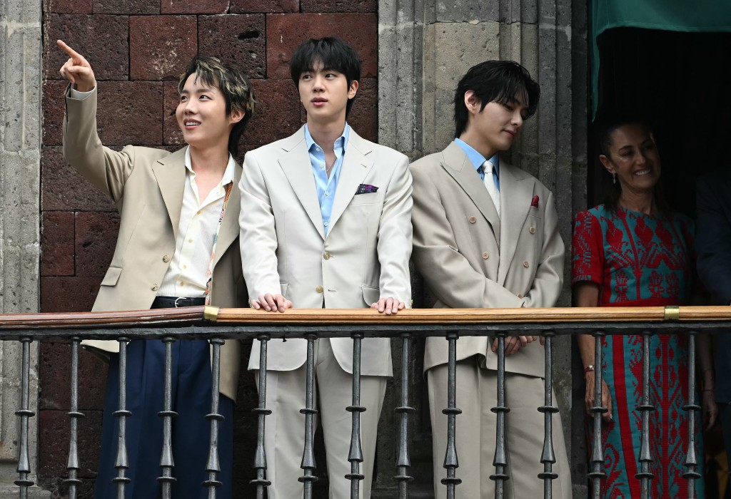 Photo by YURI CORTEZ / AFP  Hope, Jin and V from South Korean K-pop band BTS acknowledge fans past Mexico's President Claudia Sheinbaum from the balcony of the National Palace at Zocalo square in Mexico City on May 6, 2026.