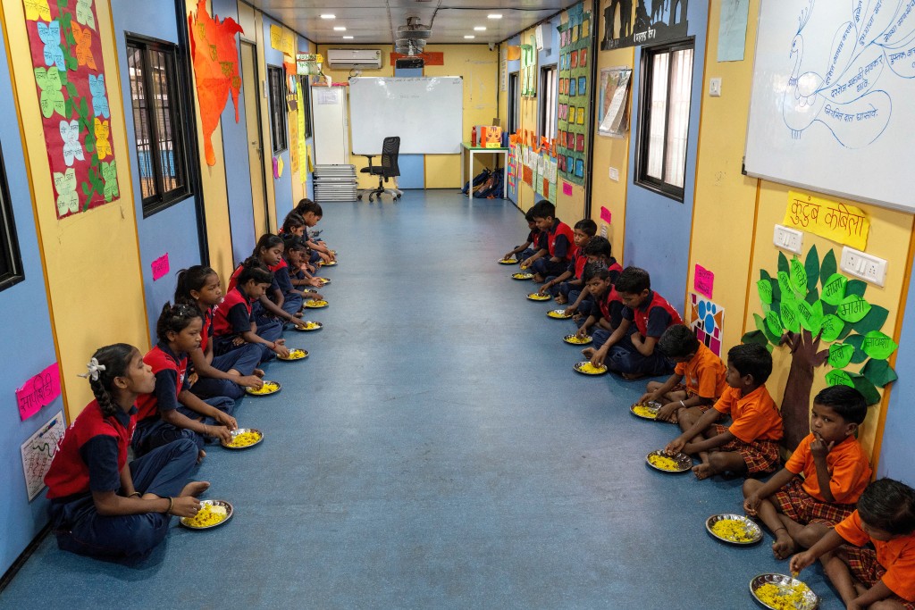 Photo by PUNIT PARANJPE / AFP  This photograph taken on May 18, 2026 shows children having their breakfast at the "Signal Shala", or traffic signal school, under a bridge in Mumbai.