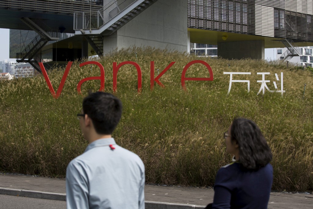 Employees walk past a logo of Vanke at its headquarters in Shenzhen, south China's Guangdong province, November 2, 2015.  REUTERS/Tyrone Siu