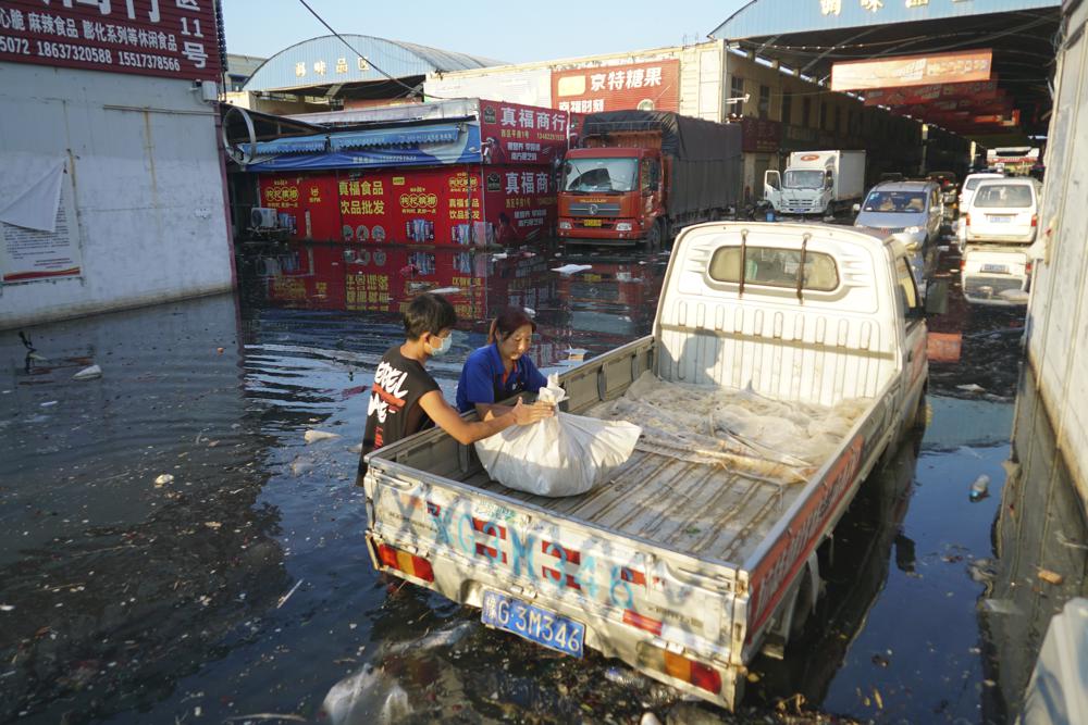 Xing, right, a shop owner at Yubei Agricultural and Aquatic Products World, wraps her goods in a plastic bag at the market in Xinxiang in central China's Henan Province, Monday, July 26, 2021. 