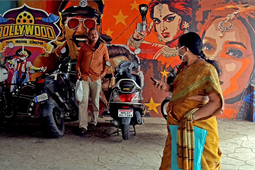 People walking past a wall mural with images of Bollywood actors, under a road bridge in Mumbai. (AFP)