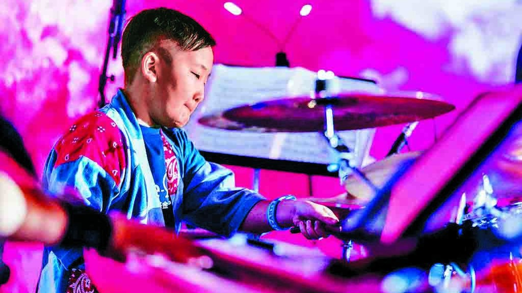 Jarvis, a wish child from Hong Kong, performs drums on stage. Make-A-Wish