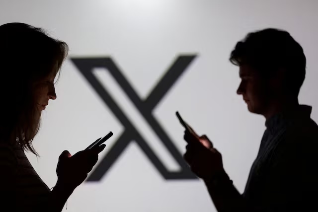 Teenagers pose for a photo while holding smartphones in front of a X logo in this illustration taken September 11, 2025. REUTERS/Dado Ruvic/Illustration/File Photo