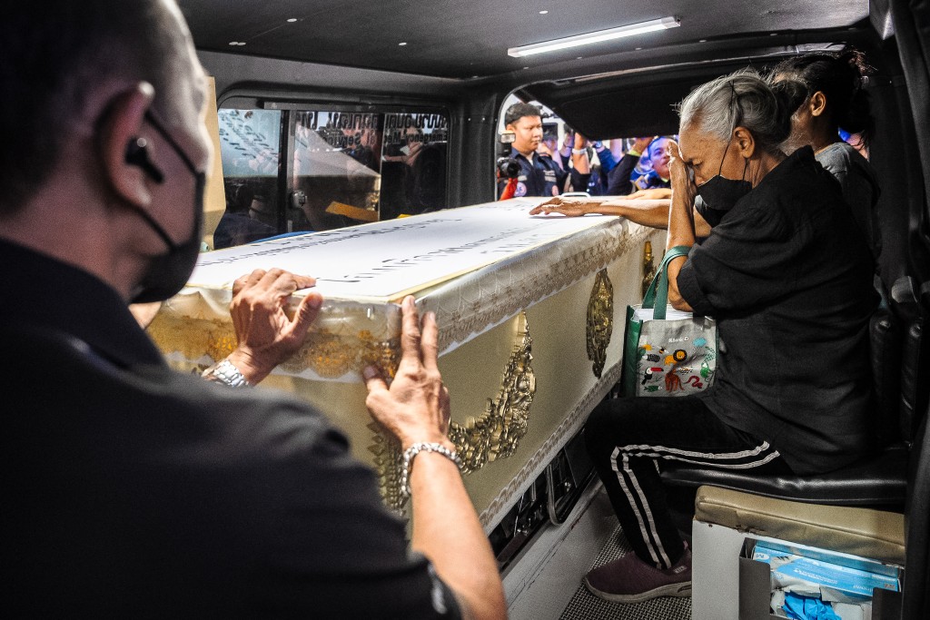 Photo by CHANAKARN LAOSARAKHAM / AFP  A relative (R) mourns next to a coffin bearing the remains of a victim killed in a bar fire, inside a hearse at the Police General Hospital in Bangkok on July 14, 2026.