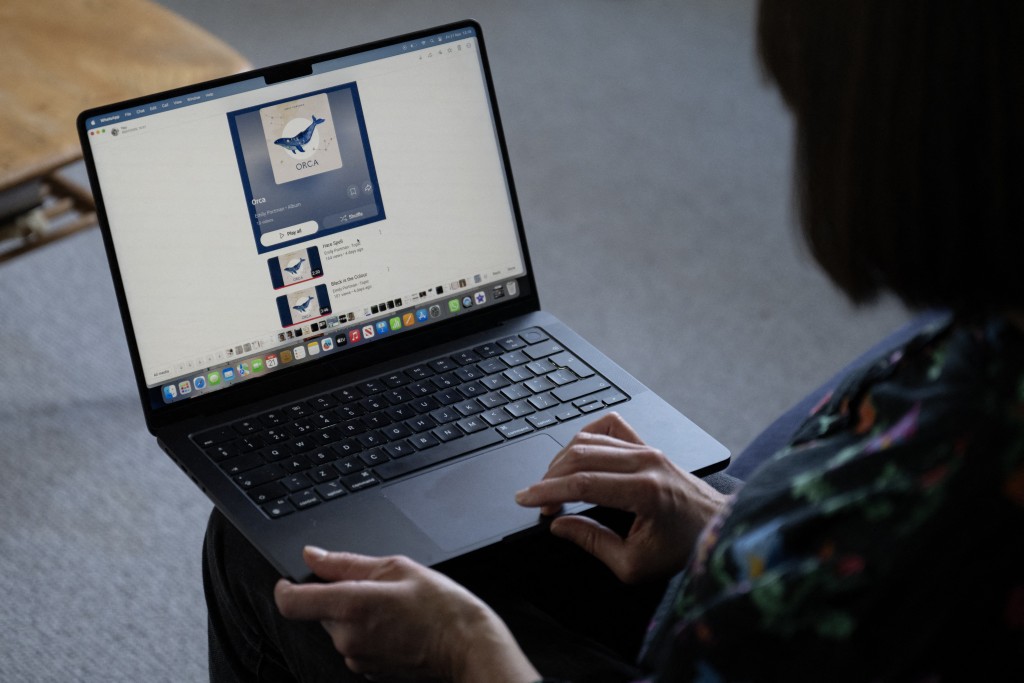 Photo by OLI SCARFF / AFP. Folk singer Emily Portman poses for a photograph holding a laptop displaying a screenshot of a counterfeit album falsely claiming to be created by her in Sheffield, northern England, on November 21, 2025.