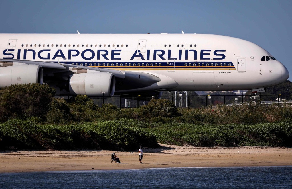 A fisherman stands on a small beach as he watches a Singapore Airlines Airbus A380 plane preparing to take-off at Sydney International Airport on September 4, 2024. AFP