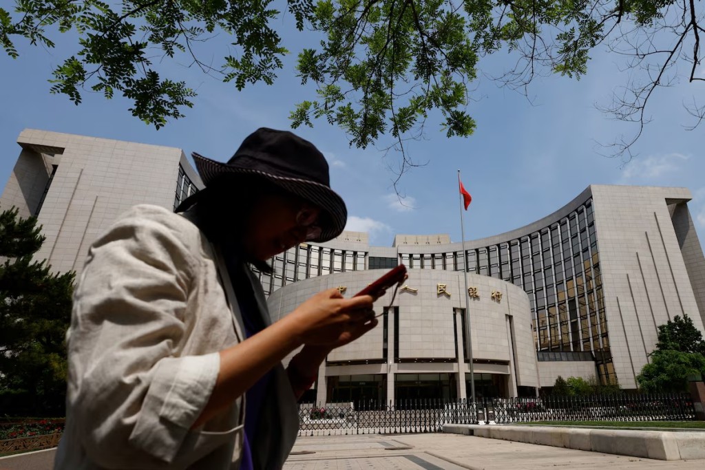 A woman uses phone as she walks past the headquarters of the People's Bank of China, in Beijing, China May 7, 2025. REUTERS
