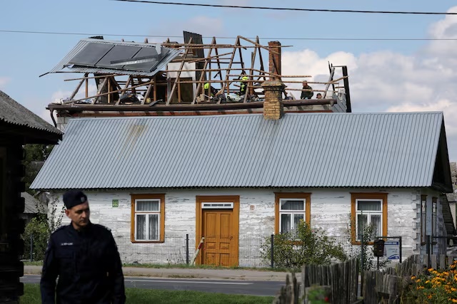 A police officer stands below as firefighters work on the destroyed roof of a house, after Russian drones violated Polish airspace during an attack on Ukraine, with some being shot down by Poland with the backing from its NATO allies, in Wyryki-Wola, Lublin Voivodeship, Poland, September 10, 2025. REUTERS/Kacper Pempel
