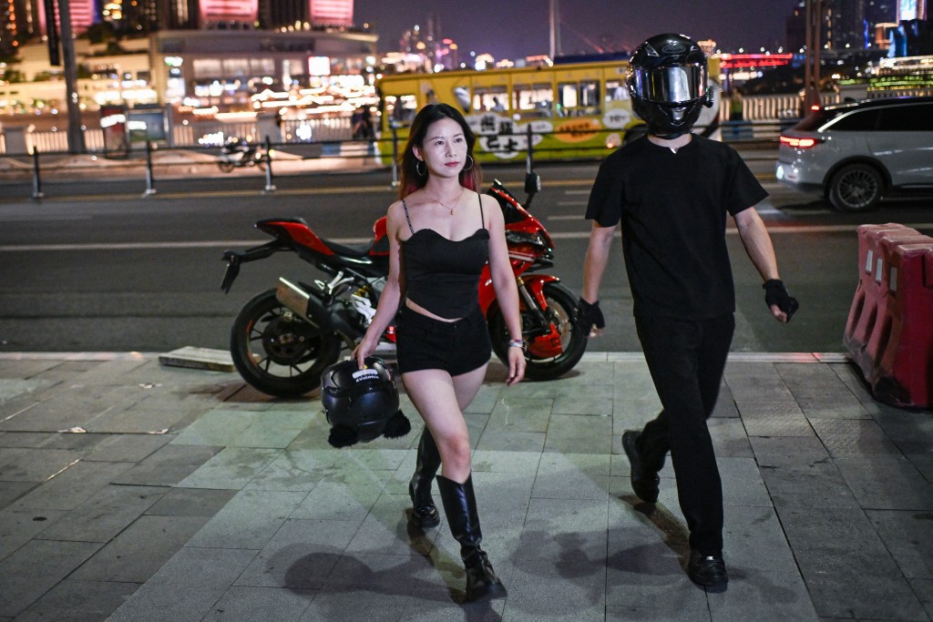 A woman posing for picture with a motorcycle rider offering photo and video service along a street in Chongqing, southwestern China. (AFP)
