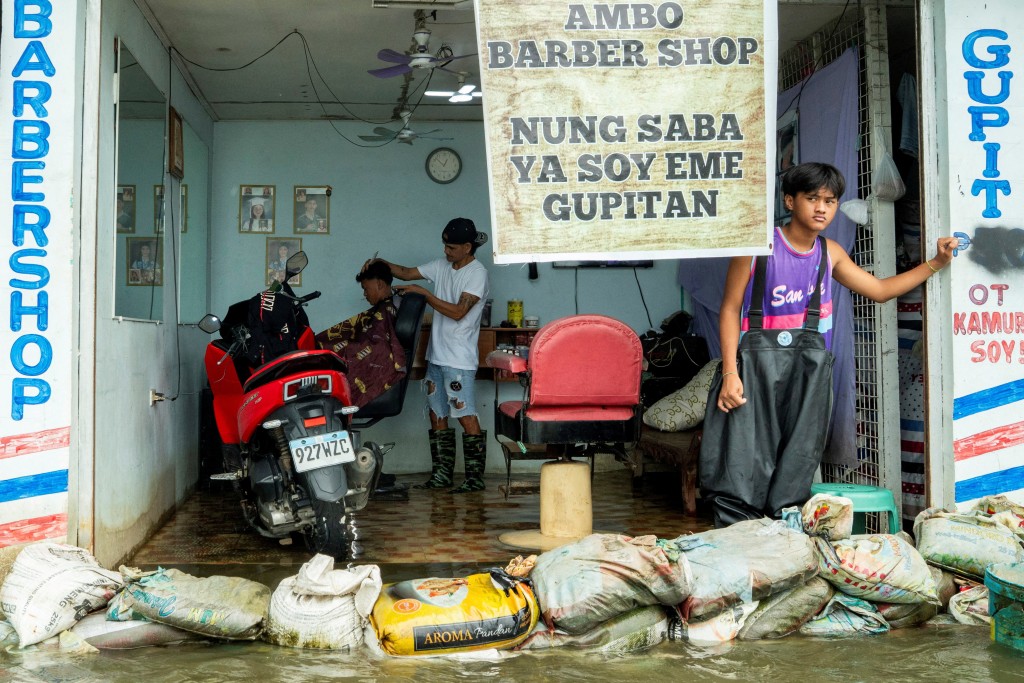 Edwardo Puno cuts a customer's hair in his flooded barbershop, following heavy rains intensified by Super Typhoon Ragasa, in Apalit, Pampanga province, Philippines, September 23, 2025. REUTERS/Lisa Marie David TPX IMAGES OF THE DAY