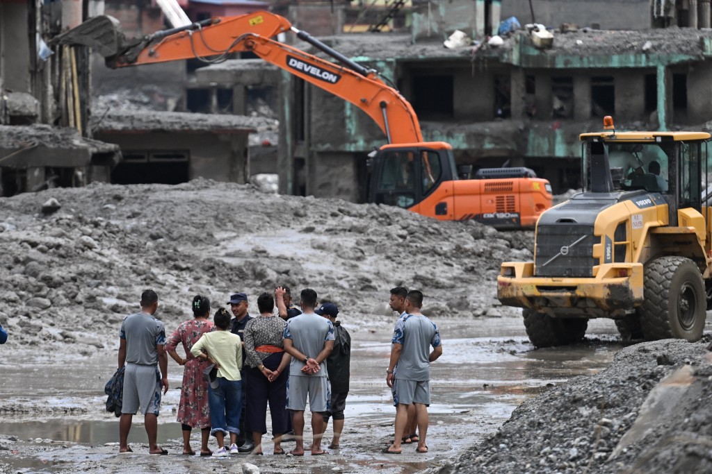 Photo by ARUN SANKAR / AFP. Residents watch as an excavator (top) helps people to collect some of their belongings from their house in the aftermath of flash floods at Trishuli, in Nepal's Nuwakot district on August 29, 2026.