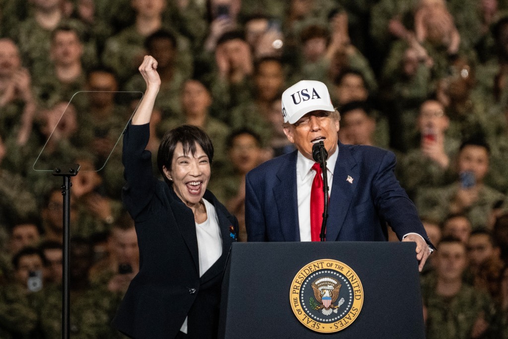 Photo by PHILIP FONG / AFP Japan's Prime Minister Sanae Takaichi (L) gestures as US President Donald Trump delivers a speech in front of US Navy personnel on board the US Navy's USS George Washington aircraft carrier at the US naval base in Yokosuka on October 28, 2025.