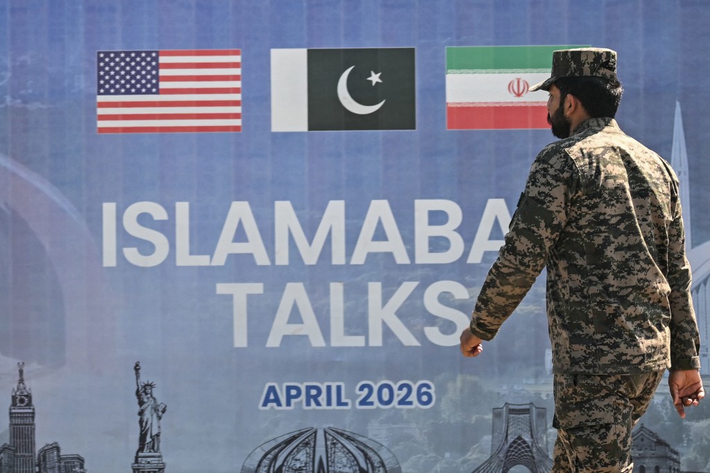 A Pakistani Ranger walks past a billboard for the US-Iran peace talks in Islamabad on April 12, 2026. (AFP)