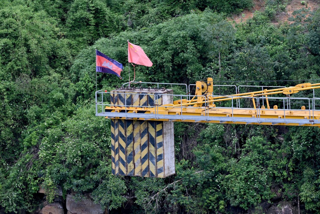 Photo by TANG CHHIN SOTHY / AFP  This photo taken on June 11, 2026 shows A Cambodian flag (L) and Chinese flag are seen on a crane at a Chinese hydrodam project company under construction at the Cardamom National Park in Koh Kong province.
