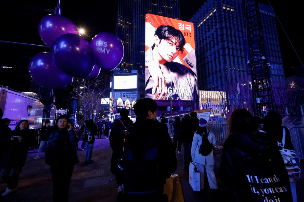 Fans of Kpop boy band BTS, known as ARMY, walk under the electronic billboard displaying BTS member Jungkook at temporarily restricted Gwanghwamun square that will be used for "BTS The Comeback Live Arirang" concert, their first performance in more than three years since completing mandatory military service, in Seoul, South Korea, March 20, 2026. REUTERS/Kim Soo-hyeon