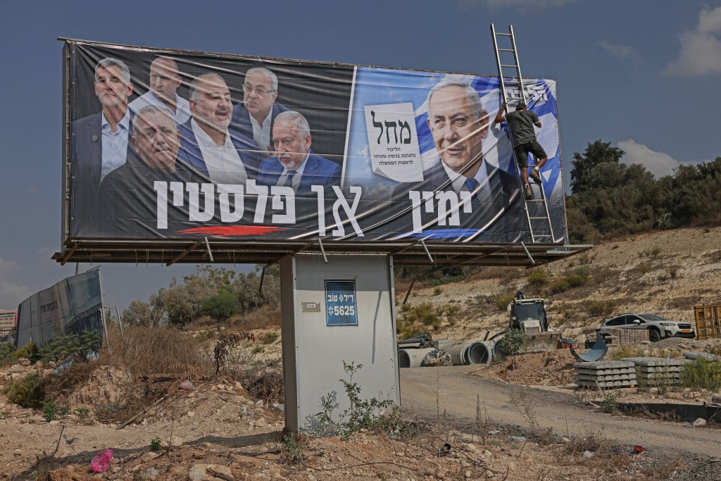 Photo by AHMAD GHARABLI / AFP  This photo taken on October 21, 2026 shows a worker unfurling on electoral campaign billboard for Israel's Prime Minister Benjamin Netanyahu's Likud party, with a Hebrew phrase reading "the Right or Palestine" alongside the faces of the members of the opposition, in Israel's northern city of Nazareth.