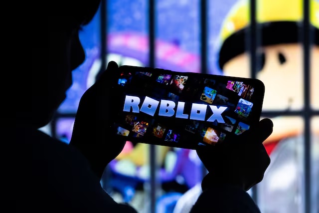A boy poses for a photo while holding a smartphone in front of a screen displaying a character of the U.S. children's video game Roblox, in this illustration taken December 8, 2025. REUTERS/Ramil Sitdikov/Illustration/File Photo