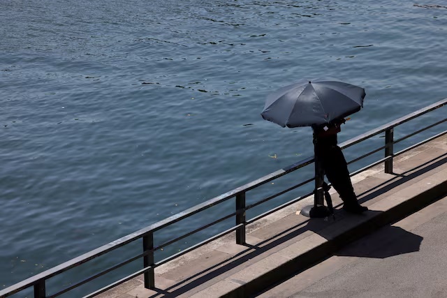 A person shelters from the sun under an umbrella along the banks of the River Seine in Paris as temperatures rise during a heatwave affecting a large part of France, June 22, 2026. REUTERS/Alice Sacco