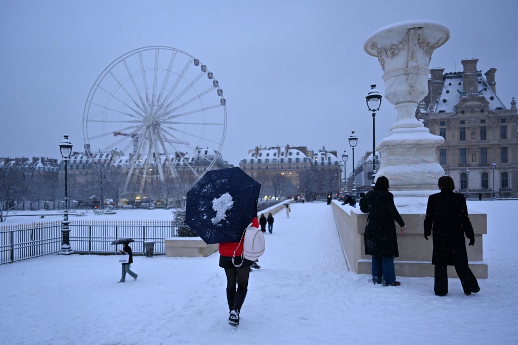 A pedestrian walks with an umbrella next to the Jardin des Tuileries covered in snow in Paris on January 5, 2026. (AFP)