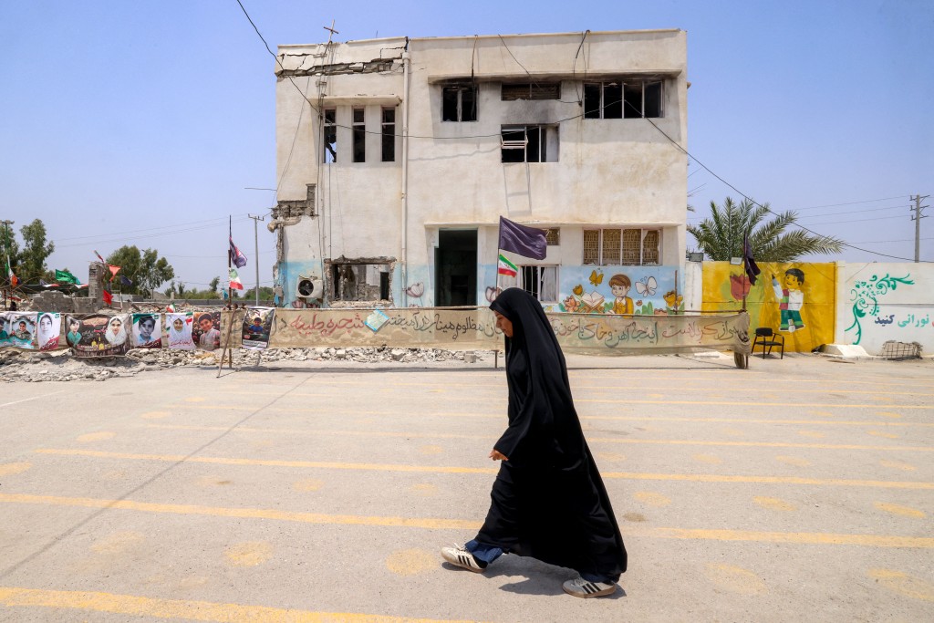 Photo by ATTA KENARE / AFP  A woman walks past the building of the destroyed Shajareh Tayebeh primary school in Minab in Iran’s Hormozgan province on August 10, 2026.