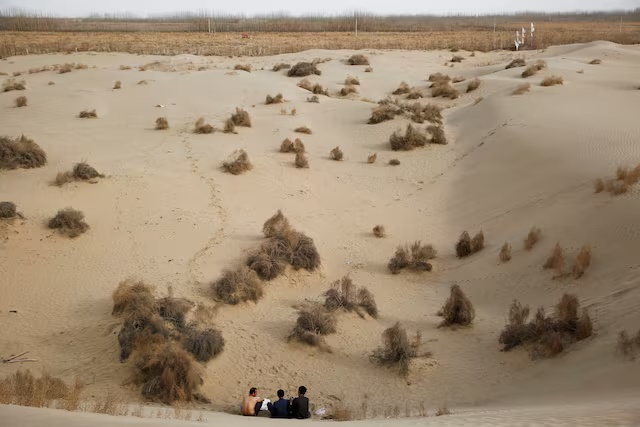 Men sit at the foot of a dune in Taklamakan Desert outside the village of Jiya near Hotan, Xinjiang Uighur Autonomous Region, China, March 21, 2017. REUTERS/Thomas Peter/File Photo