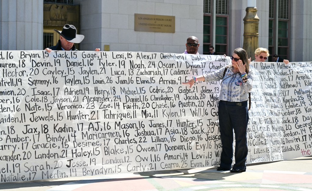 Photo by FREDERIC J. BROWN / AFP Mary Rodee, whose 15-year-old son died by suicide, points to a banner listing victims’ names outside Los Angeles Superior Court after the social media trial verdict, on March 25, 2026.