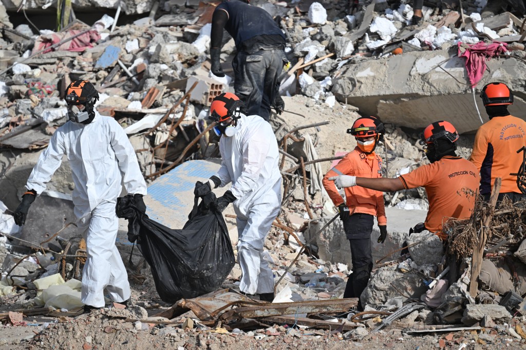 Photo by JUAN BARRETO / AFP. Forensic workers carry a body bag across the rubble of a collapsed building in Caraballeda, Venezuela, on July 17, 2026, following the June 24 earthquakes.