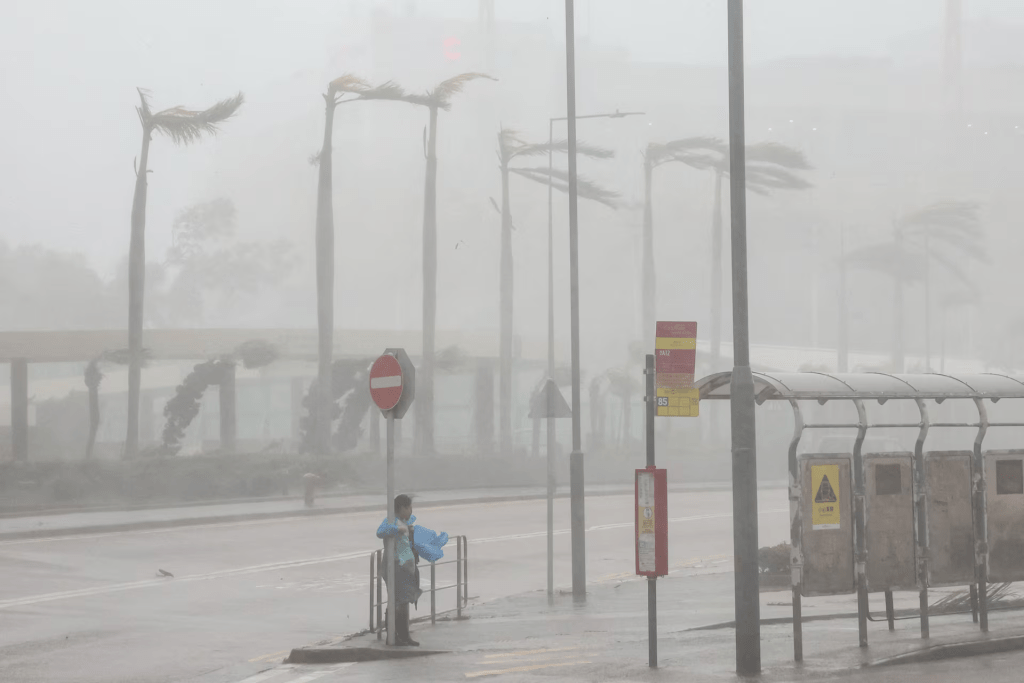 A woman clings to a traffic sign to maintain balance against strong winds from Super Typhoon Ragasa in Hong Kong, China, September 24, 2025. REUTERS/Tyrone Siu