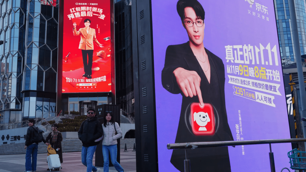 People walk by advertisement billboards promoting Chinese e-commerce platform JD.com, right, and Tmall, left, on their Singles’ Day sale at a popular shopping district in Beijing on Nov. 10, 2025. (AP Photo/Andy Wong)