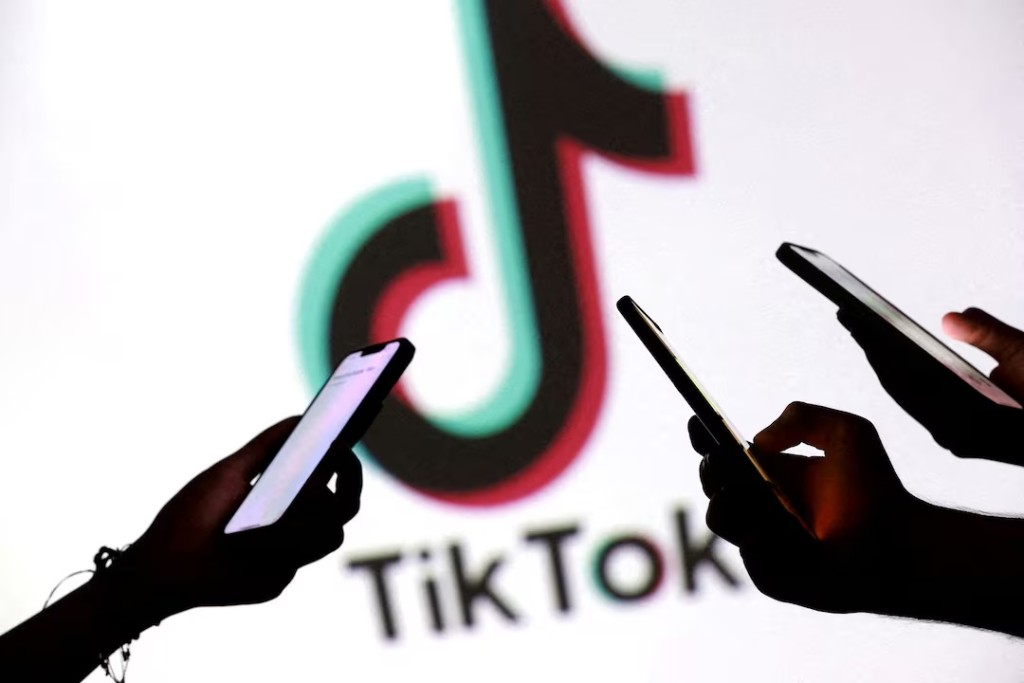 Teenagers pose for a photo while holding smartphones in front of a TikTok logo in this illustration taken September 11, 2025. REUTERS/Dado Ruvic/Illustration/File Photo