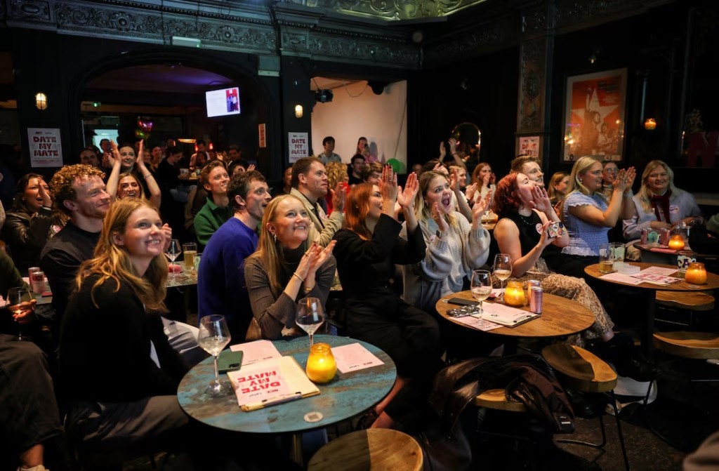  People react as they watch a presentation during “Date My Mate”, a live dating night where friends pitch their single friends, in north London, Britain, March 25, 2026. REUTERS/Isabel Infantes 