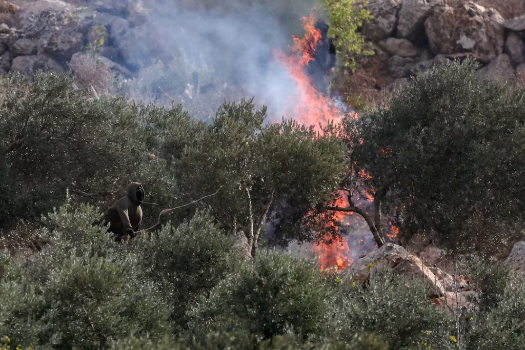 An Israeli settler casts a projectile towards Palestinians, near a fire, amid clashes during Palestinians' olive harvest in Abu Falah near Ramallah in the Israeli-occupied West Bank, October 16, 2026. REUTERS/Ammar Awad