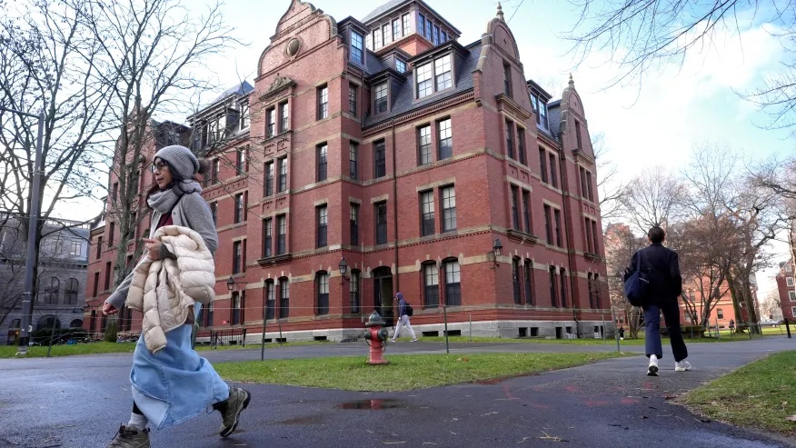 FILE – People walk between buildings, Dec. 17, 2024, on the campus of Harvard University in Cambridge, Mass. (AP Photo/Steven Senne, File)