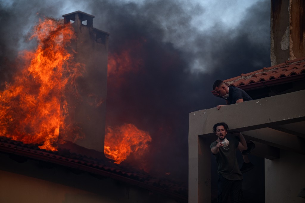 Local residents try to extinguish the fire of a burning house during a wildfire in Kryoneri, near Athens on July 26, 2025. (AFP)