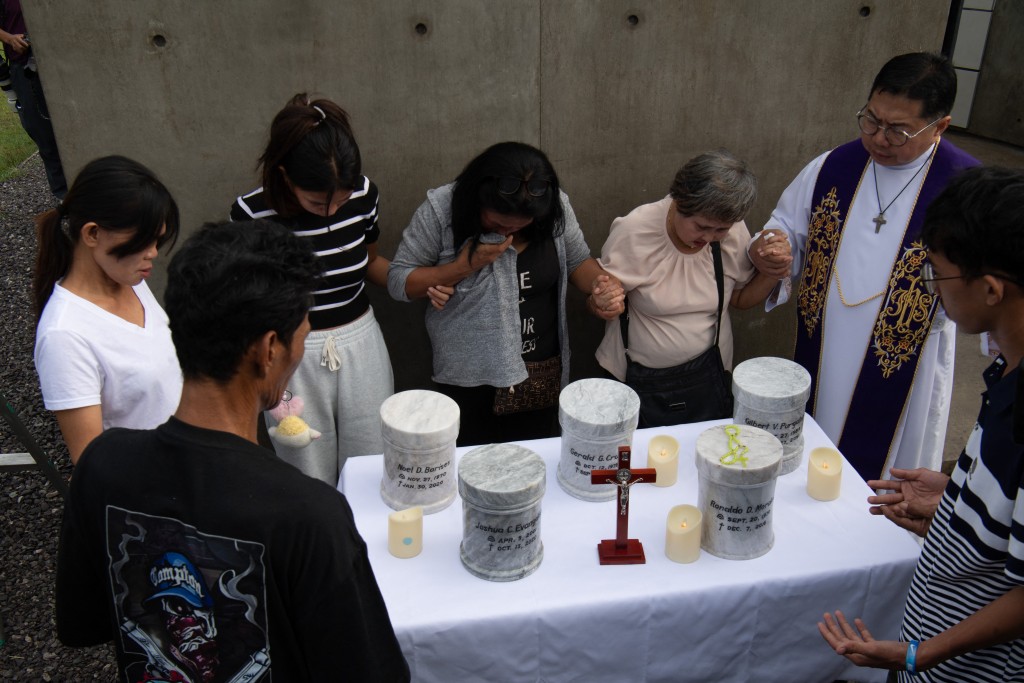 Photo by TED ALJIBE / AFP  Catholic priest Father Flavie Villanueva (R) joins hands with relatives of extrajudicial killings of former Philippine president Rodrigo Duterte's drug war during the inurnment rites at the "Dambana ng Paghilom" (Shrine of Healing) at a cemetery in Caloocan city, suburban Manila on February 20, 2026.
