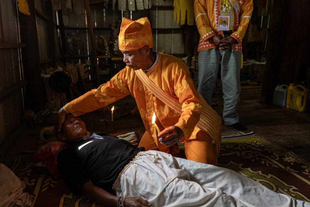 Photo by LUKE DUGGLEBY / COURTESY OF LUKE DUGGLEBY / AFP  This handout courtesy of Luke Duggleby taken on December 10, 2025 and released to AFP on February 25, 2026 shows Lahu elder and religious leader Jaha Satae (C) undertaking a drug cleansing ceremony on Jawa Jabo (black shirt), 70, who has struggled with methamphetamine and opium addiction for many years, in the village of Mae Haeng in Chiang Mai's Mae Ai district.
