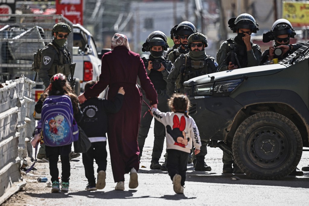 Photo by ZAIN JAAFAR / AFP  Commuters walk past members of Israeli security forces during a military raid in the neighbourhood of Kafr Aqab near Ramallah, in the Israeli-occupied West Bank on January 26, 2026.