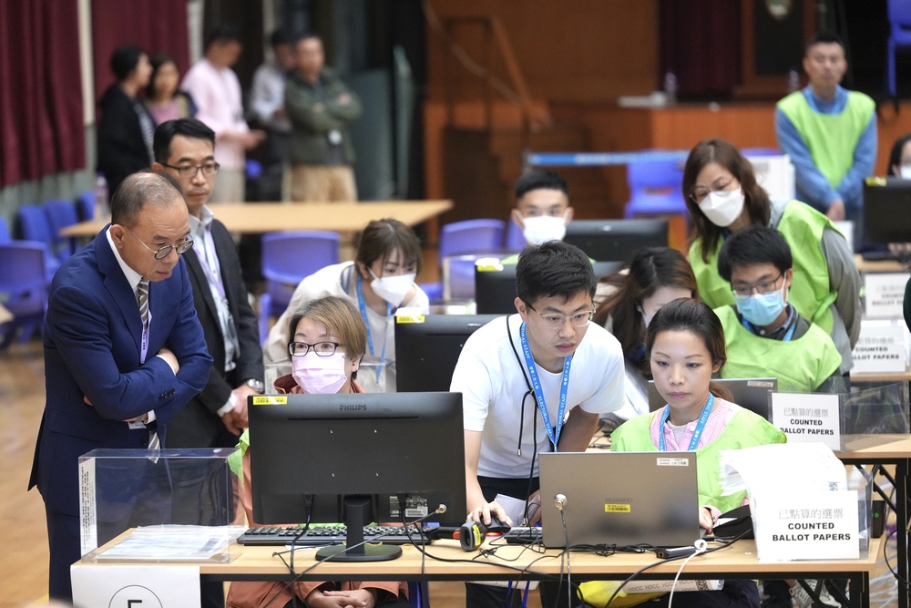 Mainland affairs chief Erick Tsang, far left, checks on staff at a counting center as Chief Executive John Lee and EAC member Bernard Man, right, empty a ballot box. SING TAO Mainland affairs chief Erick Tsang, far left, checks on staff at a counting center as Chief Executive John Lee and EAC member Bernard Man, right, empty a ballot box. SING TAO