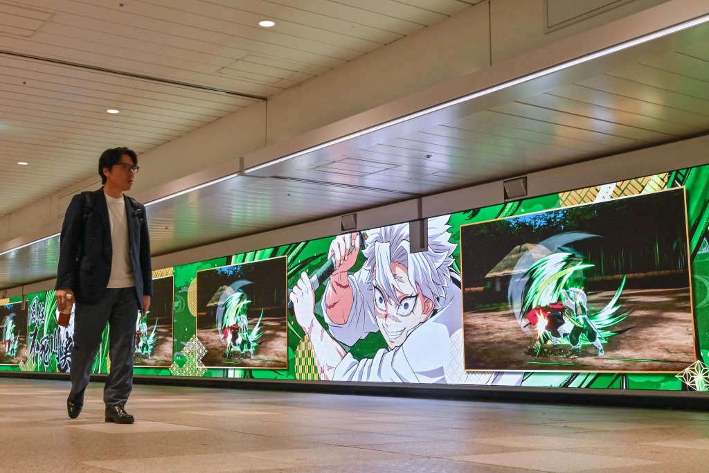 Photo by RICHARD A. BROOKS / AFP  A man walks past a long digital billboard advertising the upcoming release of the video game "Demon Slayer: Kimetsu no Yaiba – The Hinokami Chronicles 2", along a walkway inside a train station in central Tokyo on July 29, 2025.