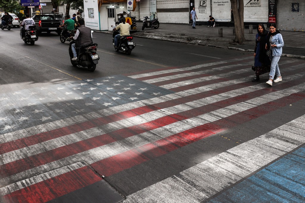 Photo by - / AFP  Iranian women walk across a painted depiction of the US flag next to an Israeli flag on a street in the south of Tehran on May 5, 2026.