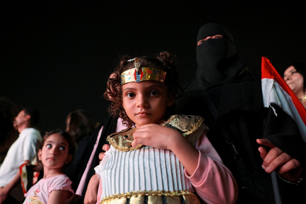 A girl wears a costume as people gather to watch the official opening ceremony of the Grand Egyptian Museum (GEM) on a big screen in the downtown area near Tahrir Square, in front of Abdeen Palace Museum, in Cairo, Egypt, November 1, 2025. (Reuters)