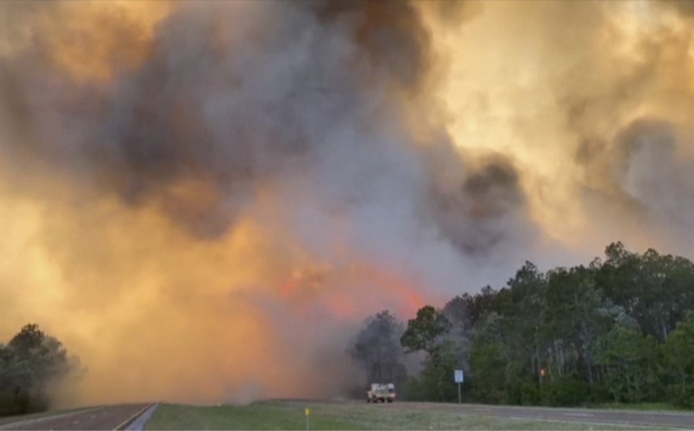 In this image made from video taken May 6, 2020 by the Florida Department of Agriculture and Consumer Services, fire and smoke rise from trees alongside a road in Santa Rosa County, Florida. In this image made from video taken May 6, 2020 by the Florida Department of Agriculture and Consumer Services, fire and smoke rise from trees alongside a road in Santa Rosa County, Florida.