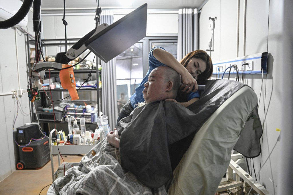 Photo by JADE GAO / AFP  This photo taken on December 16, 2025 shows Li Qian helping her elder brother Li Xia, who has Duchenne muscular dystrophy, shave his head at their house in southwestern China's Chongqing municipality.