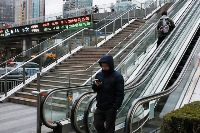 An electronic board shows Shanghai stock indices as people ride an escalator on a pedestrian bridge in the Lujiazui financial district in Shanghai, China, March 2, 2026. REUTERS/Go Nakamura/File Photo 