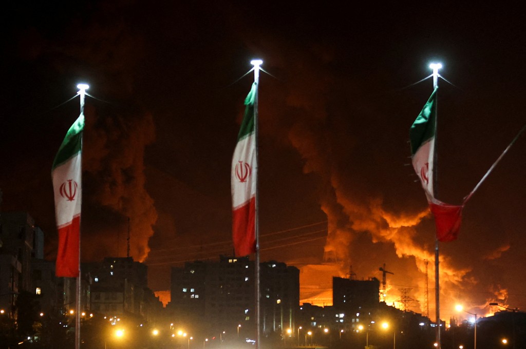 Iranian flags fly as fire and smoke from an Israeli attack on Sharan Oil depot rise, following Israeli strikes on Iran, in Tehran, Iran, June 15, 2025. (Reuters)