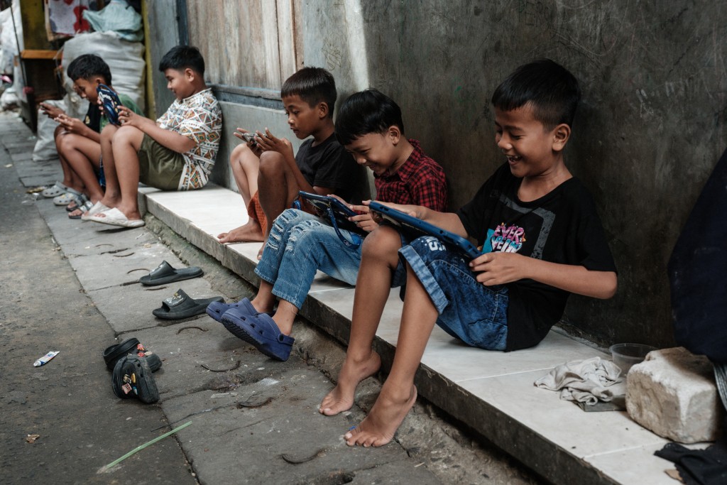 Photo by YASUYOSHI CHIBA / AFP  Children play online games against each other on smartphones and tablets along an alley in Jakarta on March 26, 2026.
