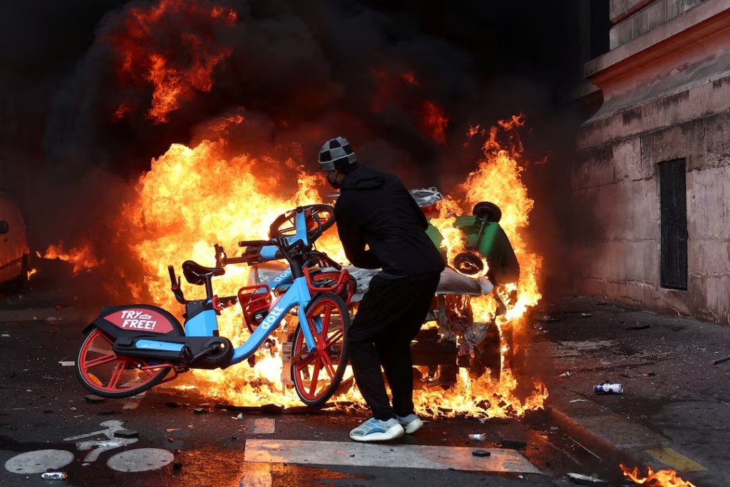 A protester throws a bicycle onto a burning car amid clashes during a day of demonstrations against the cost of living and rising fuel prices in Paris as part of nationwide protests called by the "Yellow Vests" movement, joined by French high school and university students, teachers and parents demanding better school conditions and government action, as well as labour unions, workers, farmers and retirees, France, October 17, 2026. REUTERS/Abdul Saboor/File Photo