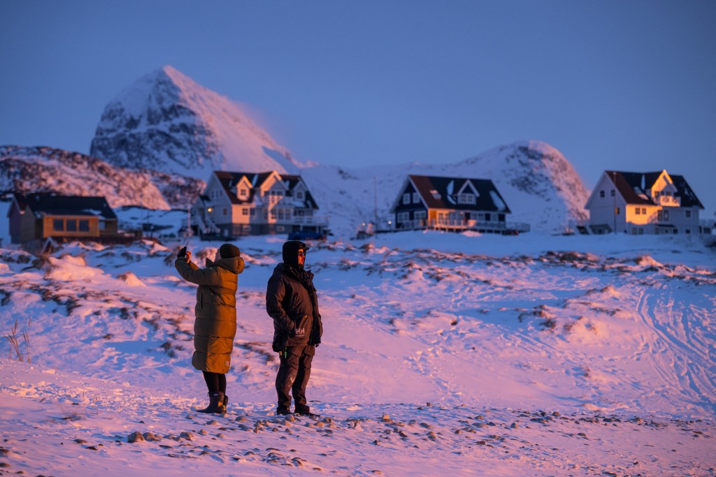 Locals stand on a snowy shoreline at dusk in Nuuk, Greenland, on January 21, 2026. (Photo by Jonathan NACKSTRAND / AFP)
