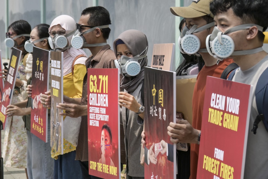 Demonstrators wearing gas masks hold protest placards outside China's embassy to demand an audit of supply chains linked to Indonesian forest fires, in Jakarta on October 22, 2026. (Photo by BAY ISMOYO / AFP)